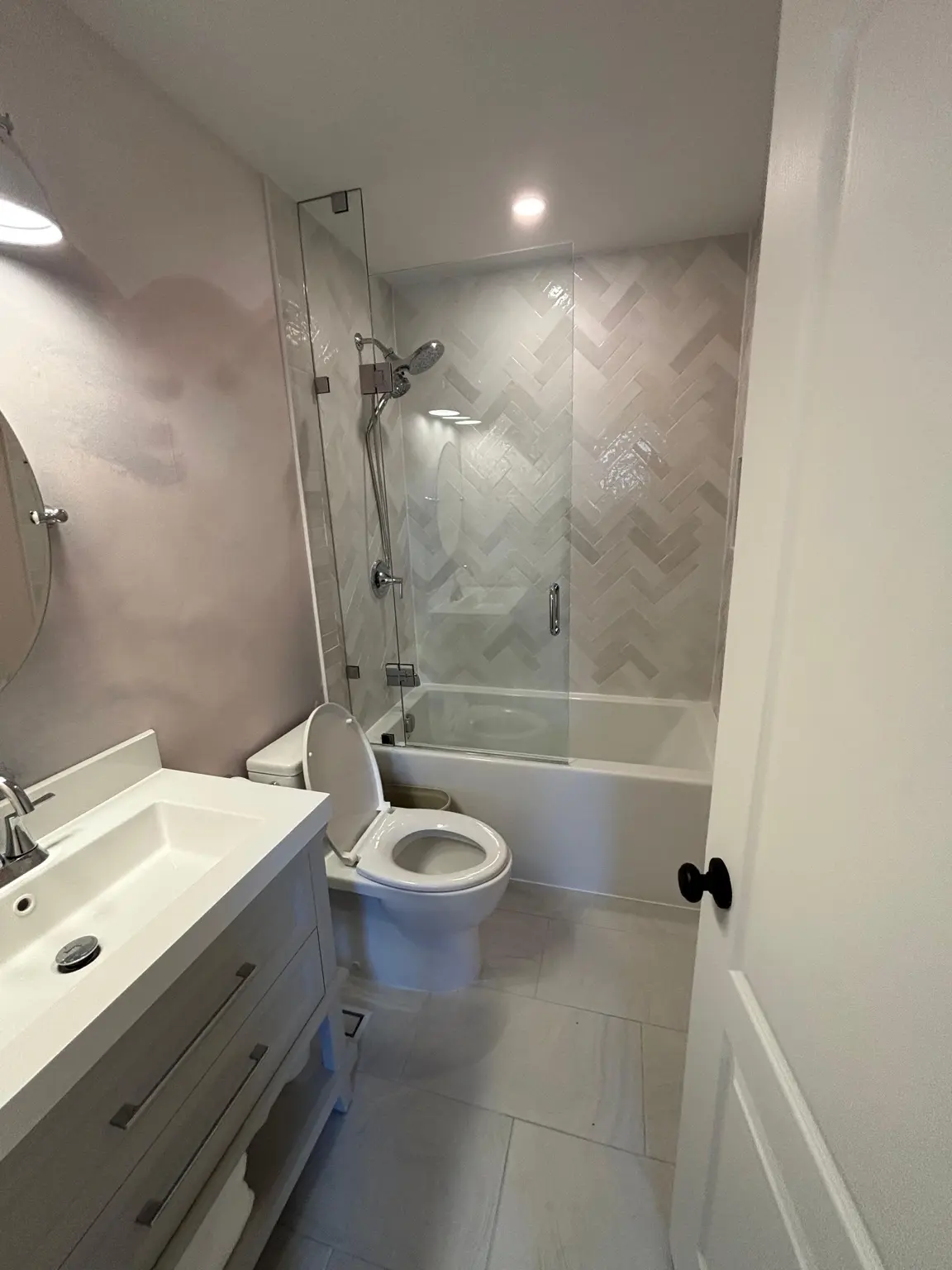 Completed compact bathroom with grey vanity, glass bath screen and herringbone wall tile