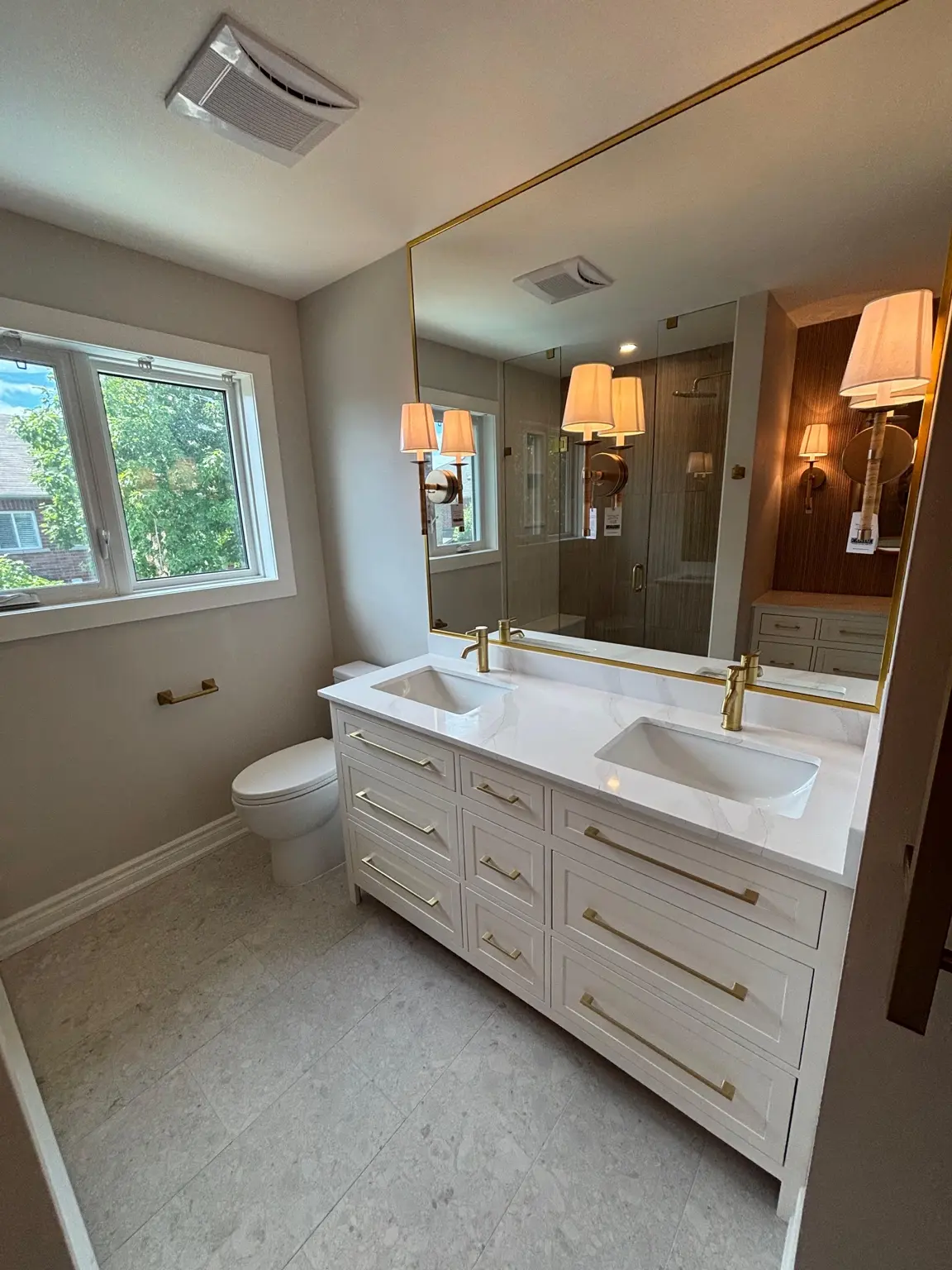 Completed bathroom with a white double vanity, brass fixtures, a large mirror and custom accent details