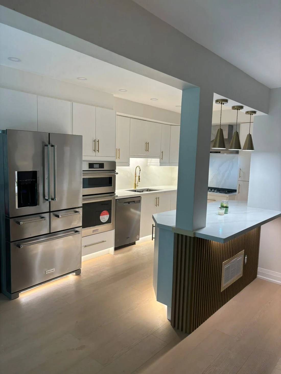 Completed kitchen with white cabinetry, integrated appliances, wood island panelling and under-cabinet lighting